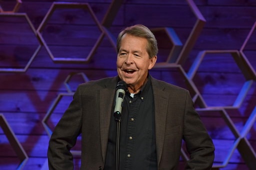 Dave Dugan performing at Dry Bar Comedy against a purple hexagonal backdrop