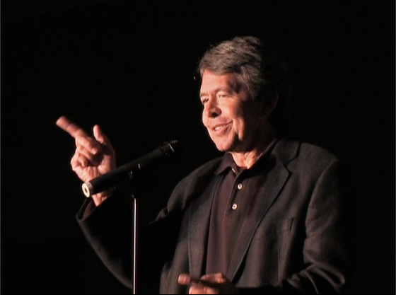 Dave Dugan performing on stage pointing at the audience with a microphone